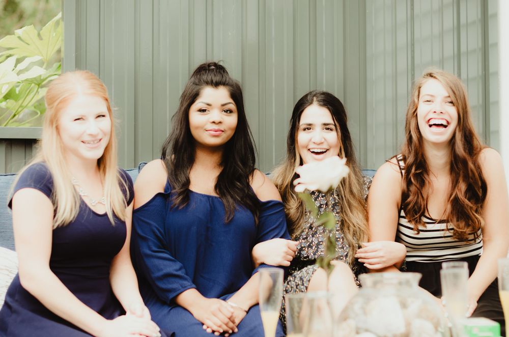 A group of friends sitting together and laughing on a porch during a casual outdoor gathering.