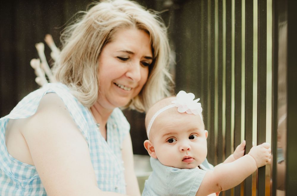 A tender parenting moment shows loving interaction between adult and infant by a railing outdoors.