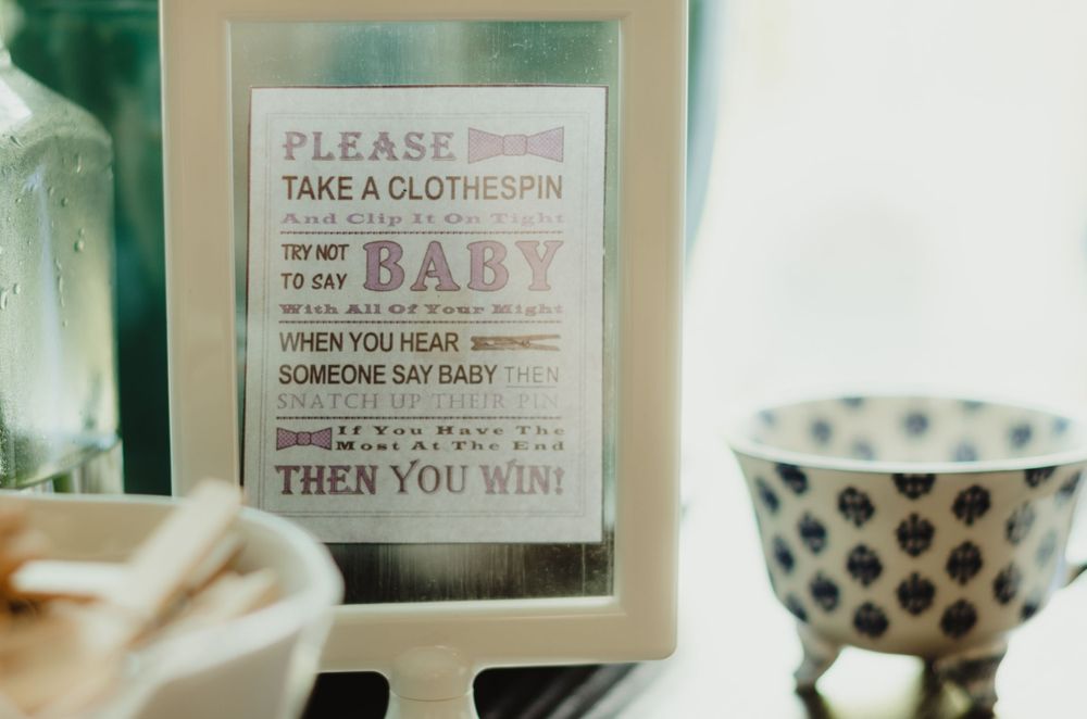 A framed motivational quote on baby laundry sits next to a polka dot teacup in a soft, muted scene.
