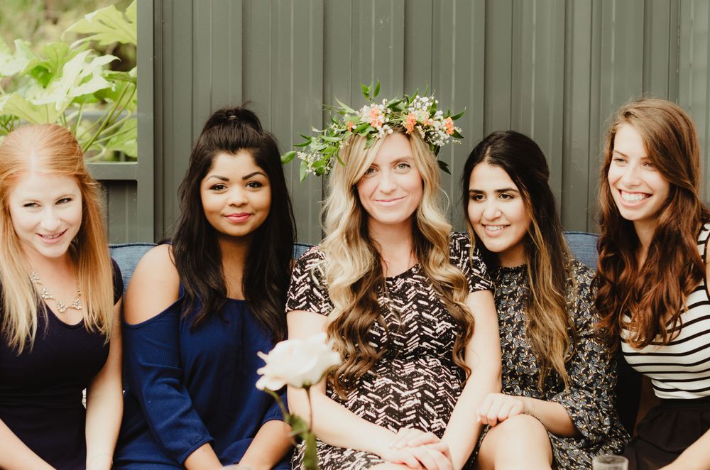 A group of five friends sitting close together outdoors wearing casual dresses and tops in varying colors and patterns.