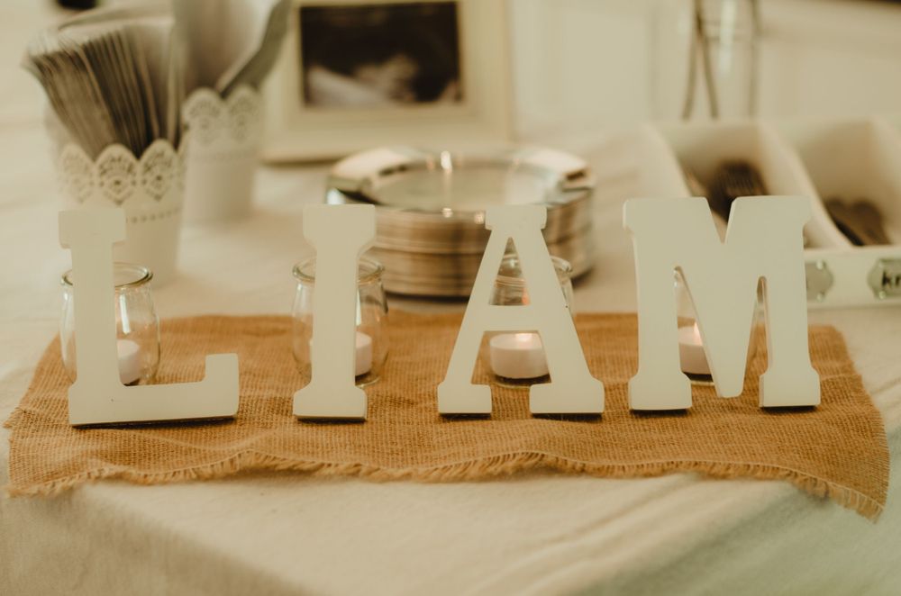 White wooden GLAM letters displayed on burlap fabric with soft vintage styling decor elements.