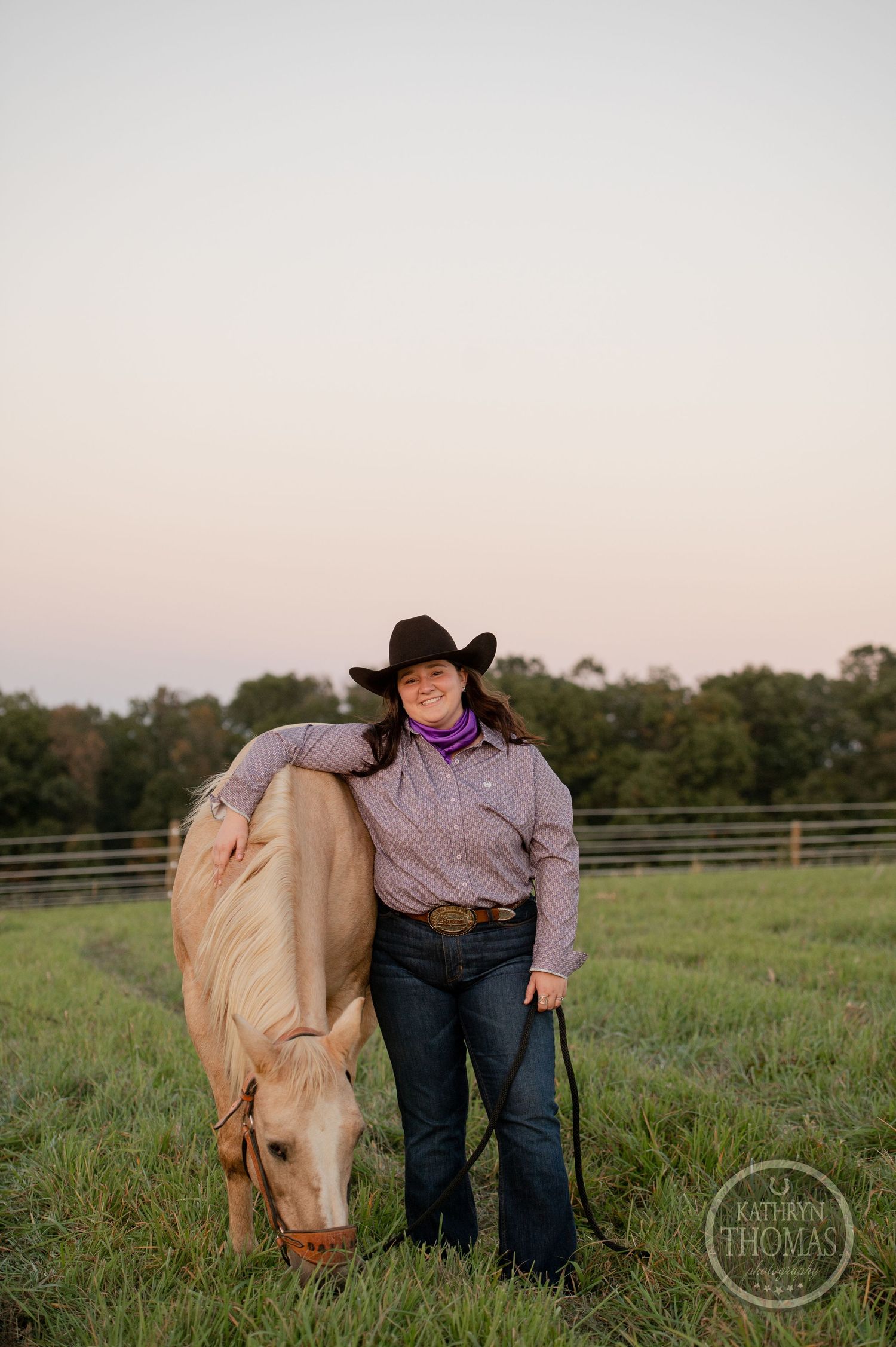 A palomino horse grazes peacefully next to its handler in a sunset-lit pasture.