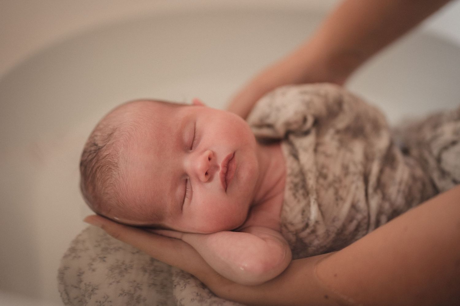 Nouveau-né paisiblement endormi, emmailloté dans un lange, est tenu pour un thérapeuthique bain bébé TBB.