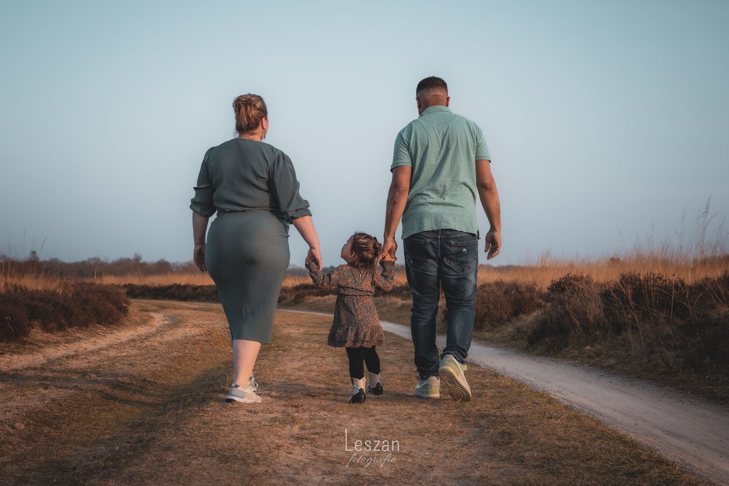 A family takes a sunset walk together on a dirt path through a rural landscape.