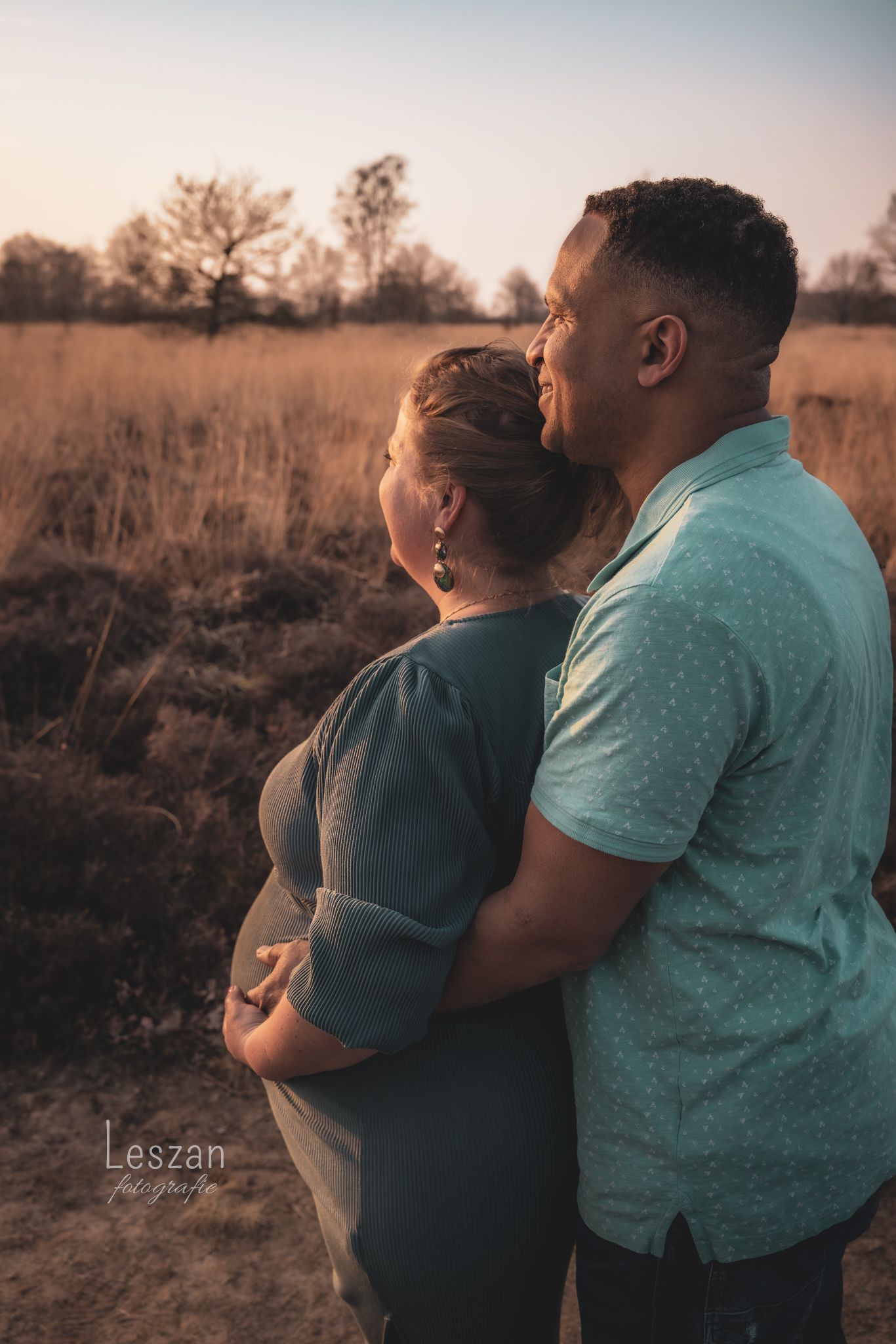 A couple embraces in a golden field at sunset, creating a warm and intimate silhouette against the natural backdrop.