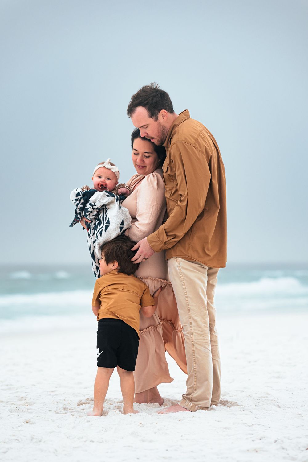 Family embracing in a tender moment while standing on white sand beach.