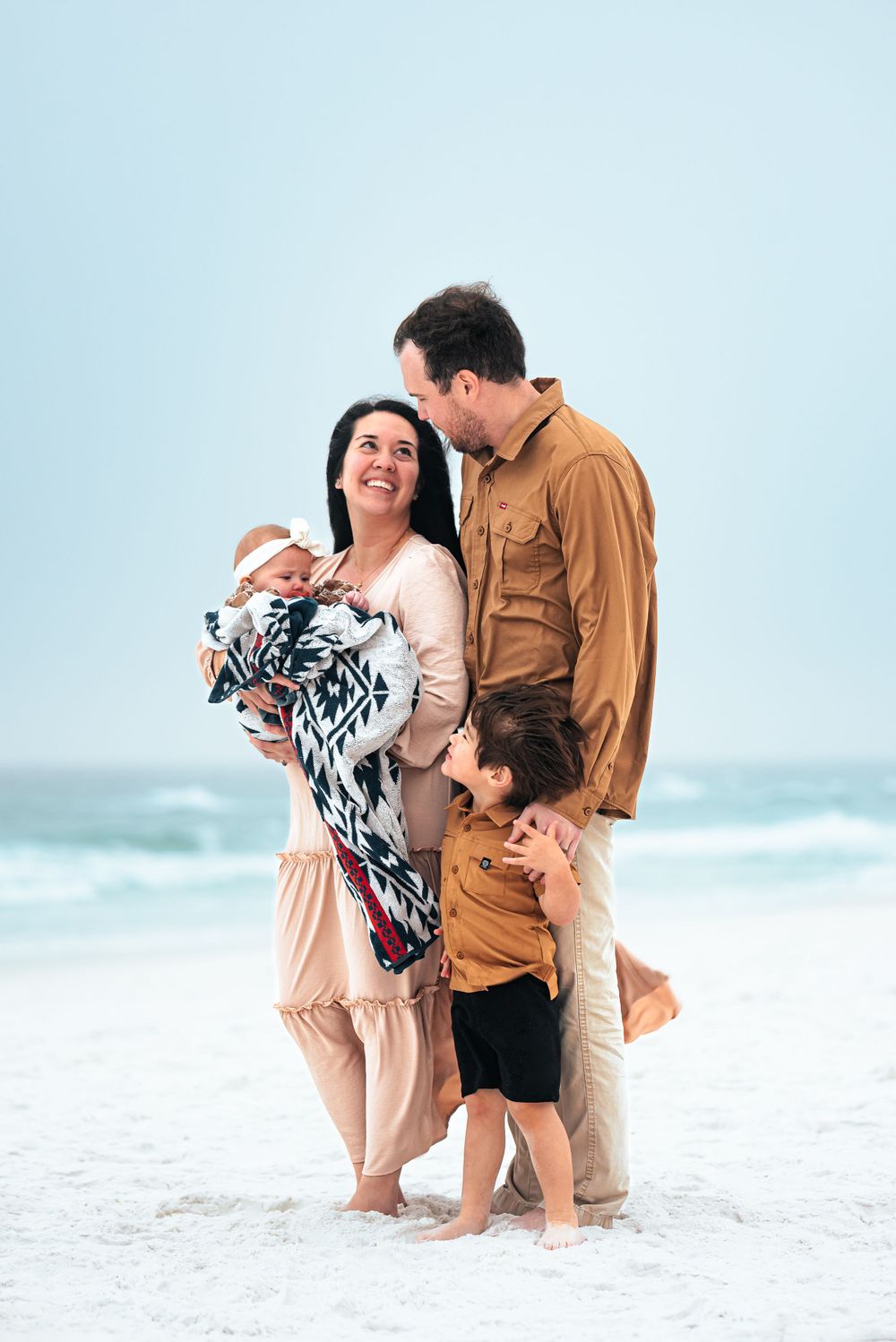 Family enjoying a tender moment together on a misty beach with coordinated outfits and soft tones.