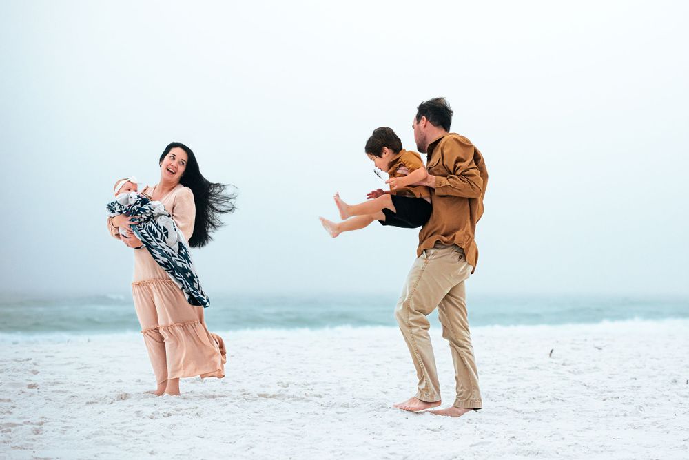 Playful family moment captured on a white sandy beach with casual clothing and joyful expressions.