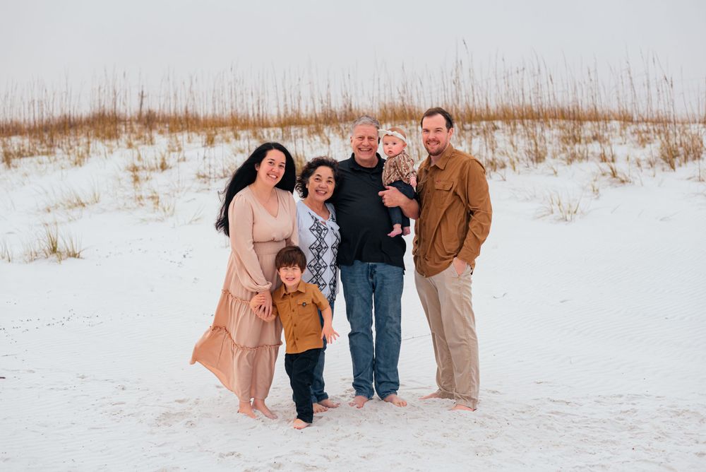 A family poses together on a white sandy beach with sea grass in the background on a cloudy day.