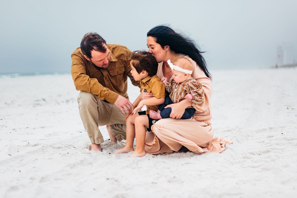 Family sharing an intimate moment while gathered close together on white sand.