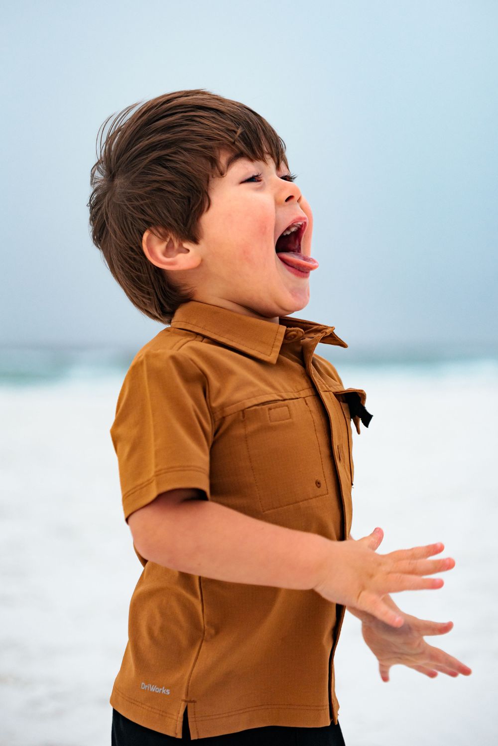 Young child in orange shirt expressing pure joy at the beach.