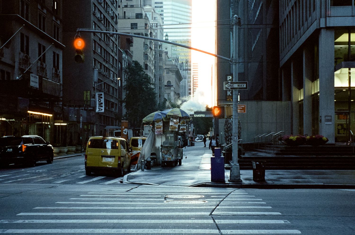 City intersection with yellow taxi and tall buildings during golden hour in New York.