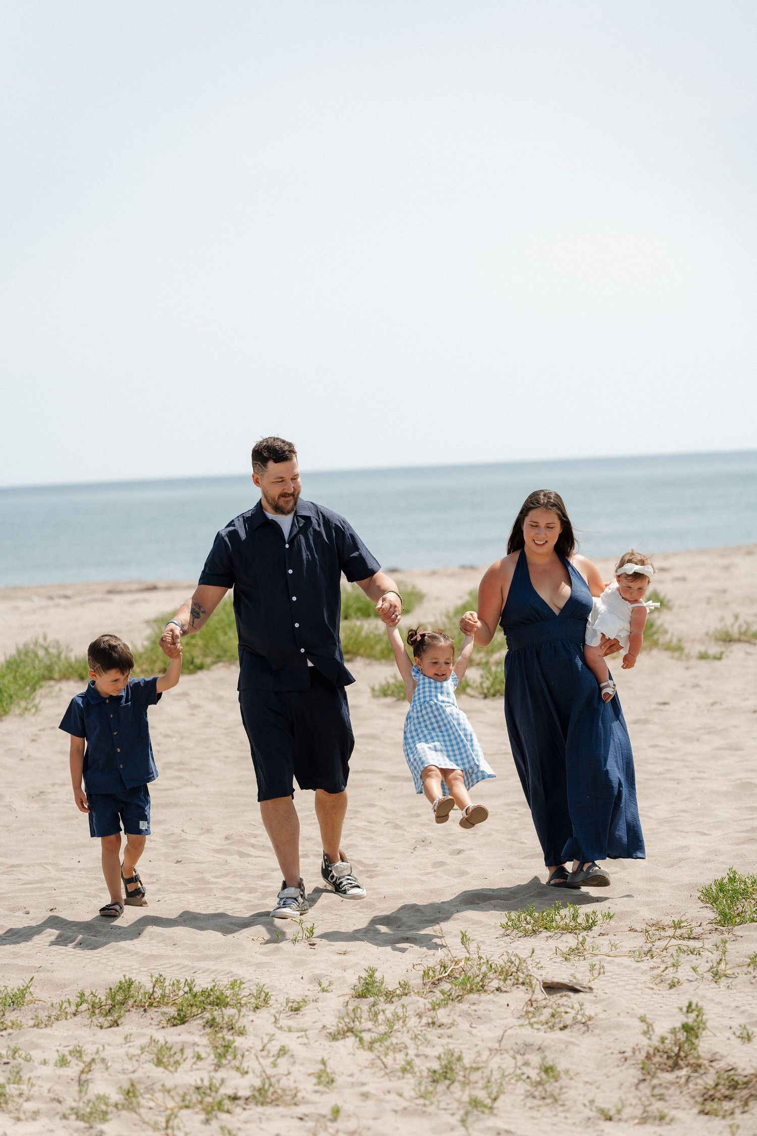 Family of five walking on Rainbow Haven Beach, parents swinging children by the hands.