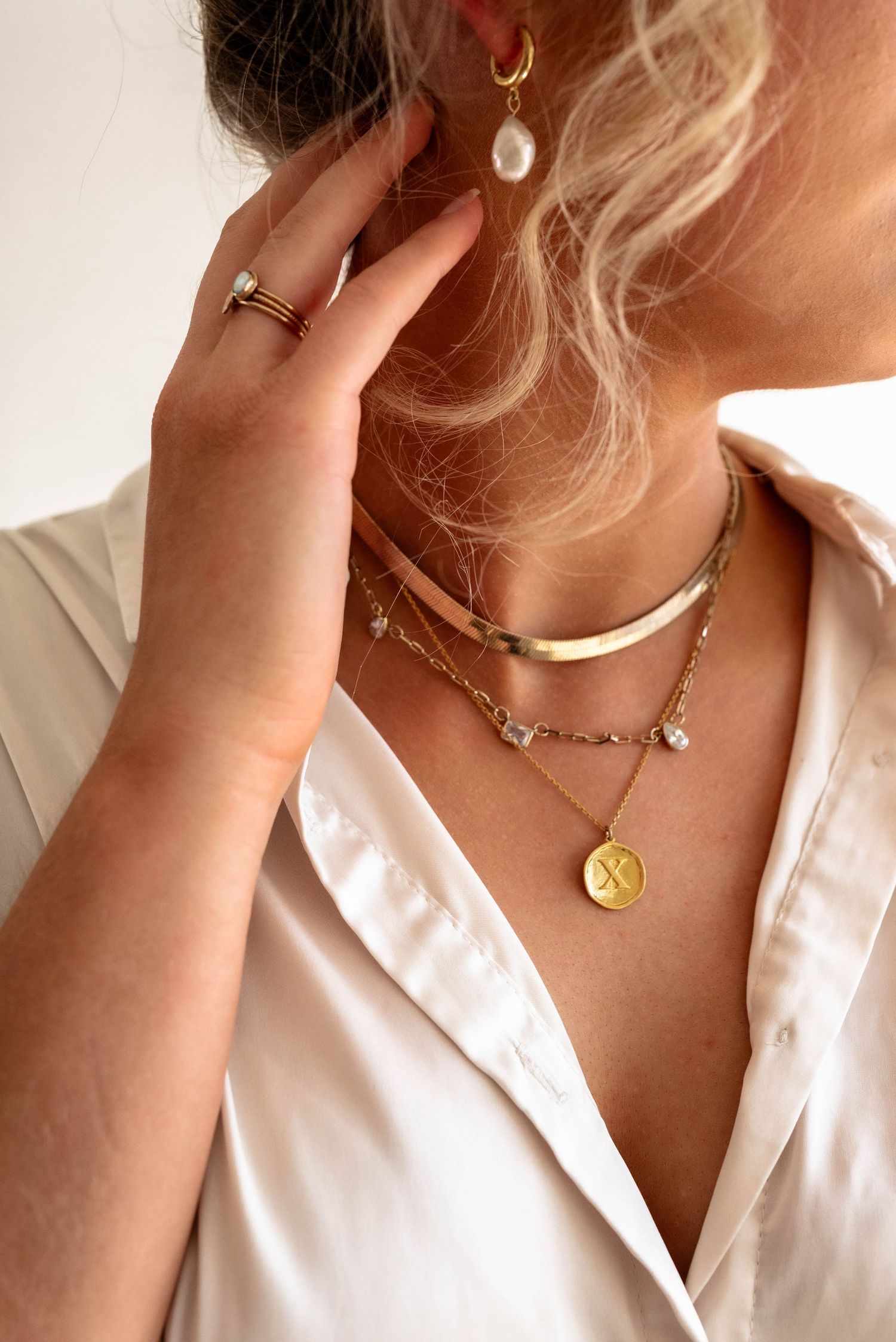 Elegant layered gold necklaces with pearl earring styled against a crisp white shirt.