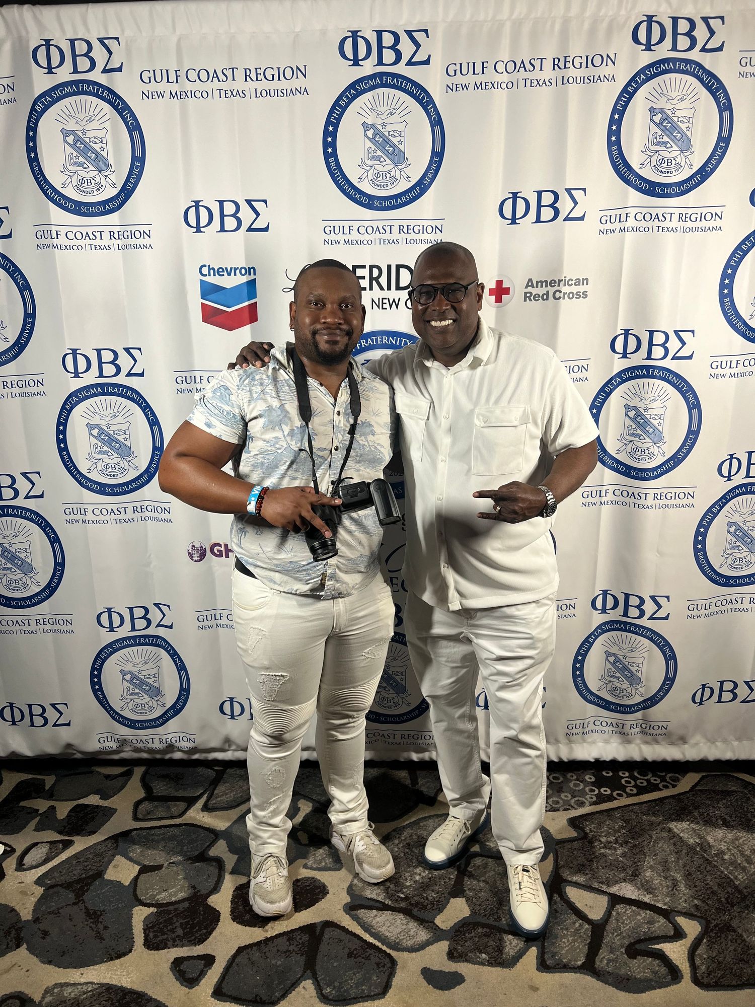 Two people posing in front of Phi Beta Sigma fraternity backdrop at formal event.