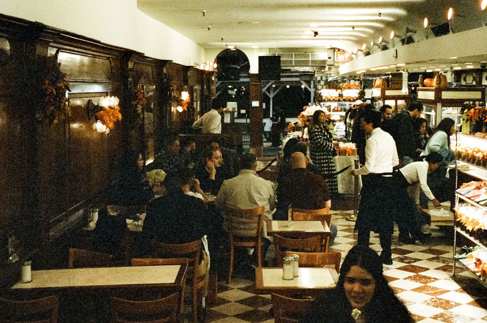 Busy vintage diner interior with customers seated at tables and counter.