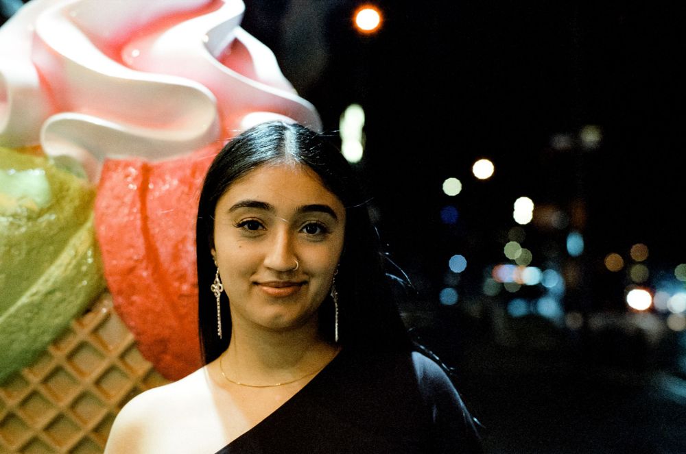 Person standing next to large decorative ice cream cone sculpture at night.