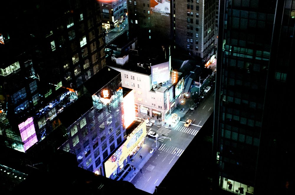 Aerial nighttime view of illuminated city streets and buildings with neon signs.