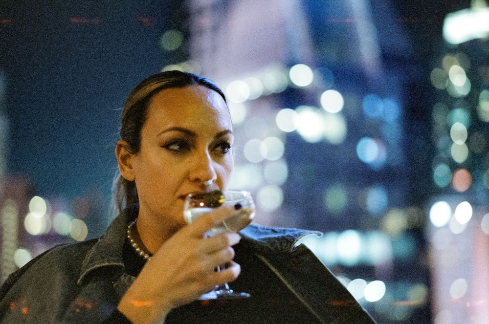 Person enjoying a cocktail against blurred city lights at night.