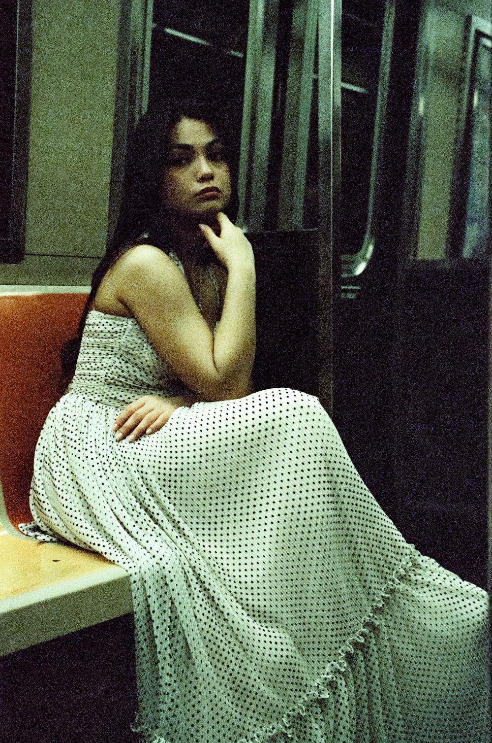 Person in polka dot dress seated on subway bench.