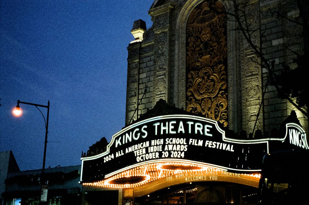 Illuminated vintage Kings Theatre marquee sign glowing against a dark blue evening sky.