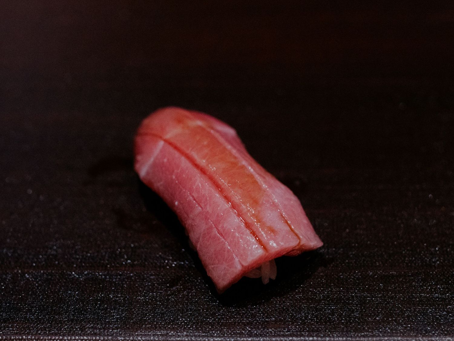 A piece of red tuna nigiri sushi on a dark surface showcasing the fresh raw fish.