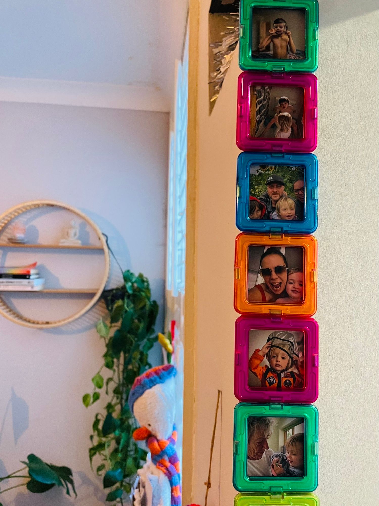 Colorful square photo frames arranged vertically on a wall with indoor plants and circular shelf in view.