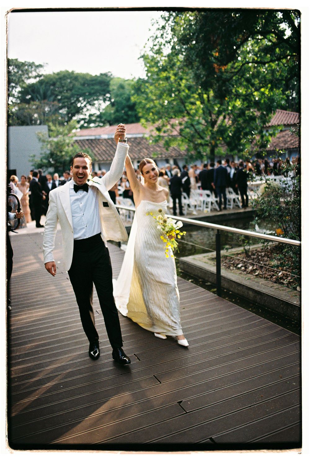 Newlyweds celebrating on wooden deck with raised hands in victory pose.