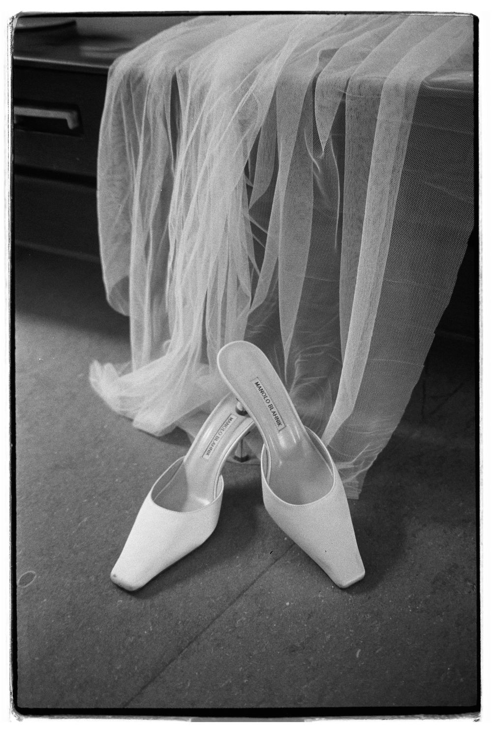 Elegant white bridal shoes and veil arranged on dark floor.