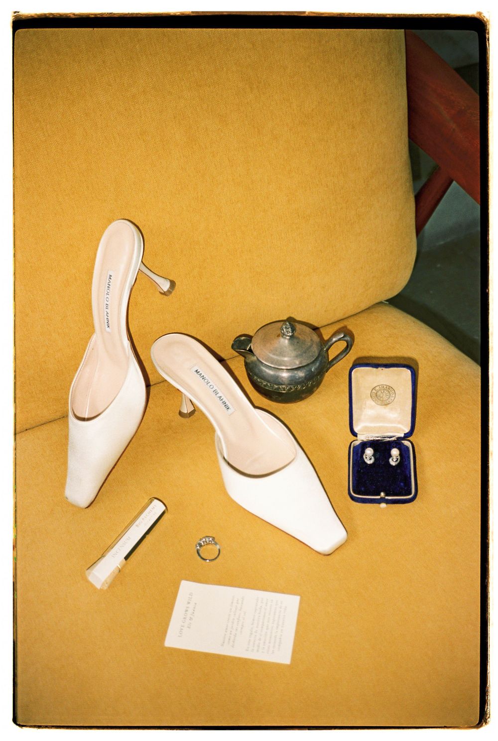 Elegant white bridal shoes arranged with jewelry box and teapot on yellow background.