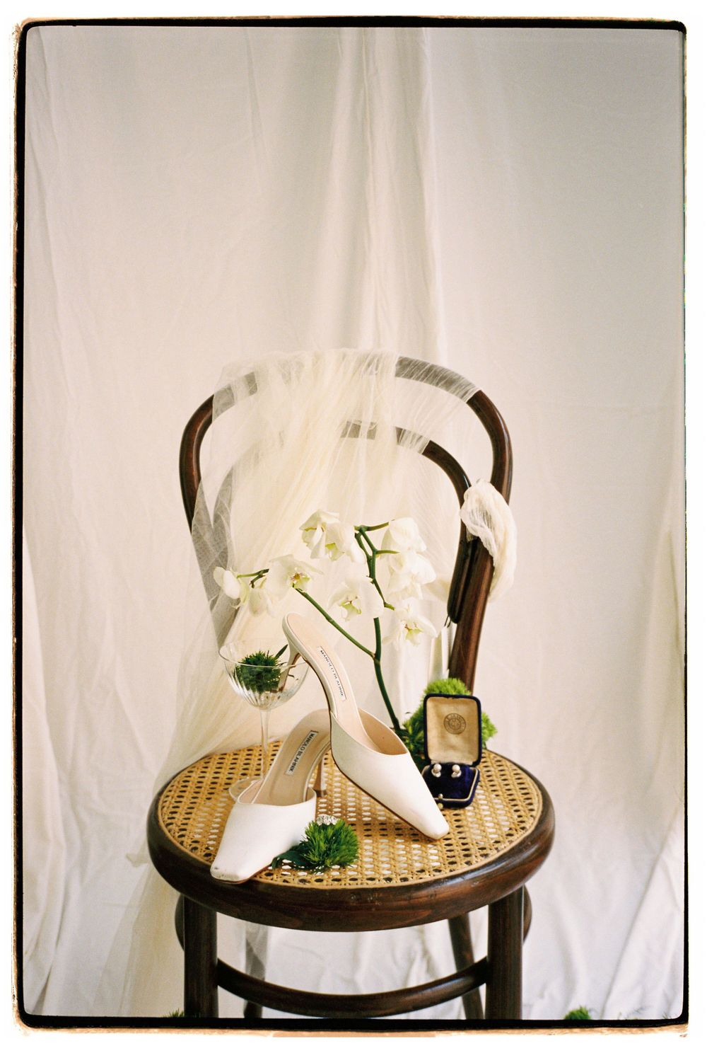 White wedding shoes and veil displayed on vintage cane chair with orchid decoration.