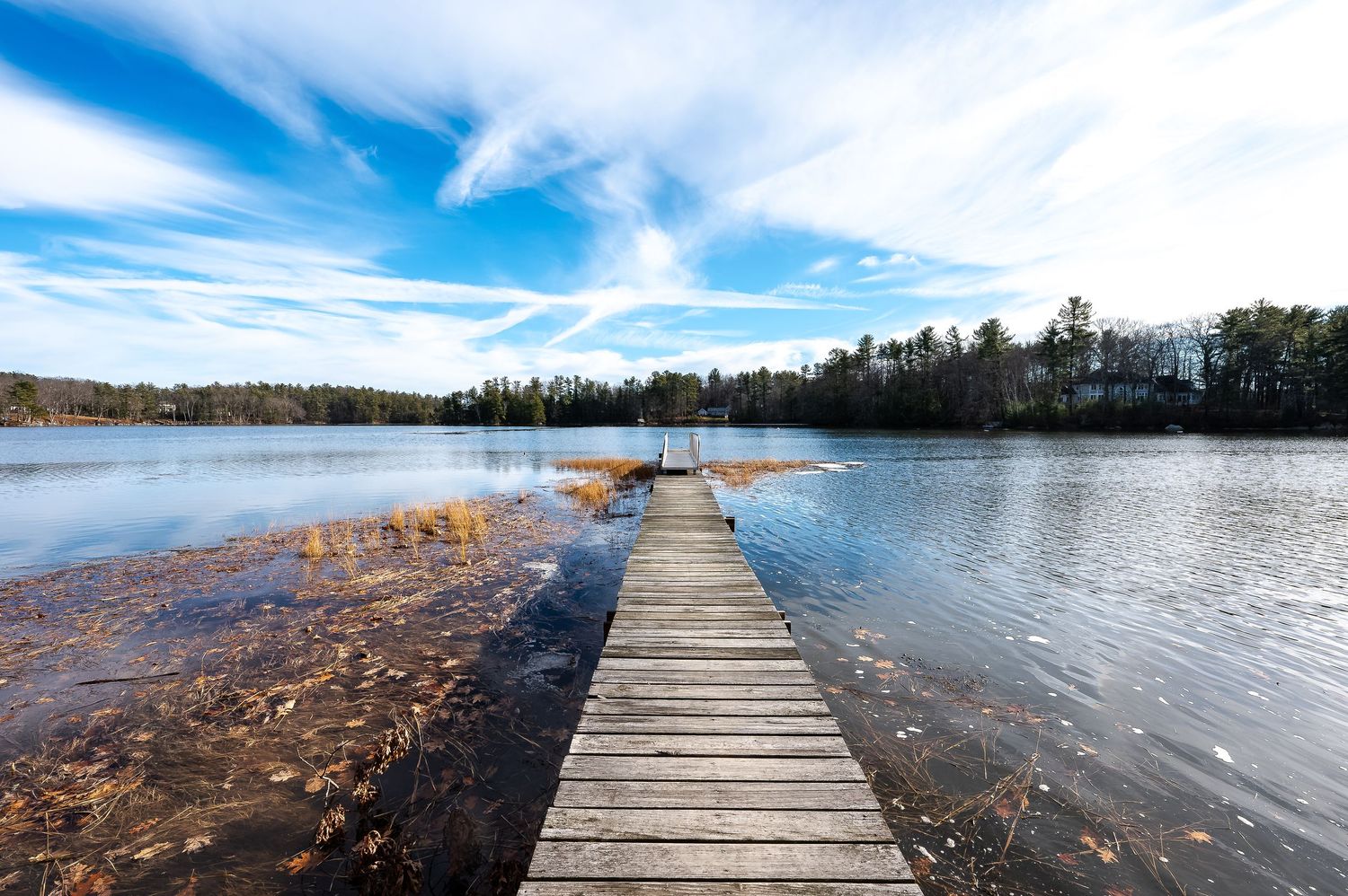 Long wooden pier stretches across lake waters under dramatic blue and white cloudy sky.
