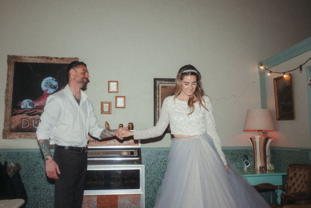 A couple dances together in a vintage-style room with a teal wall and pink lamp.
