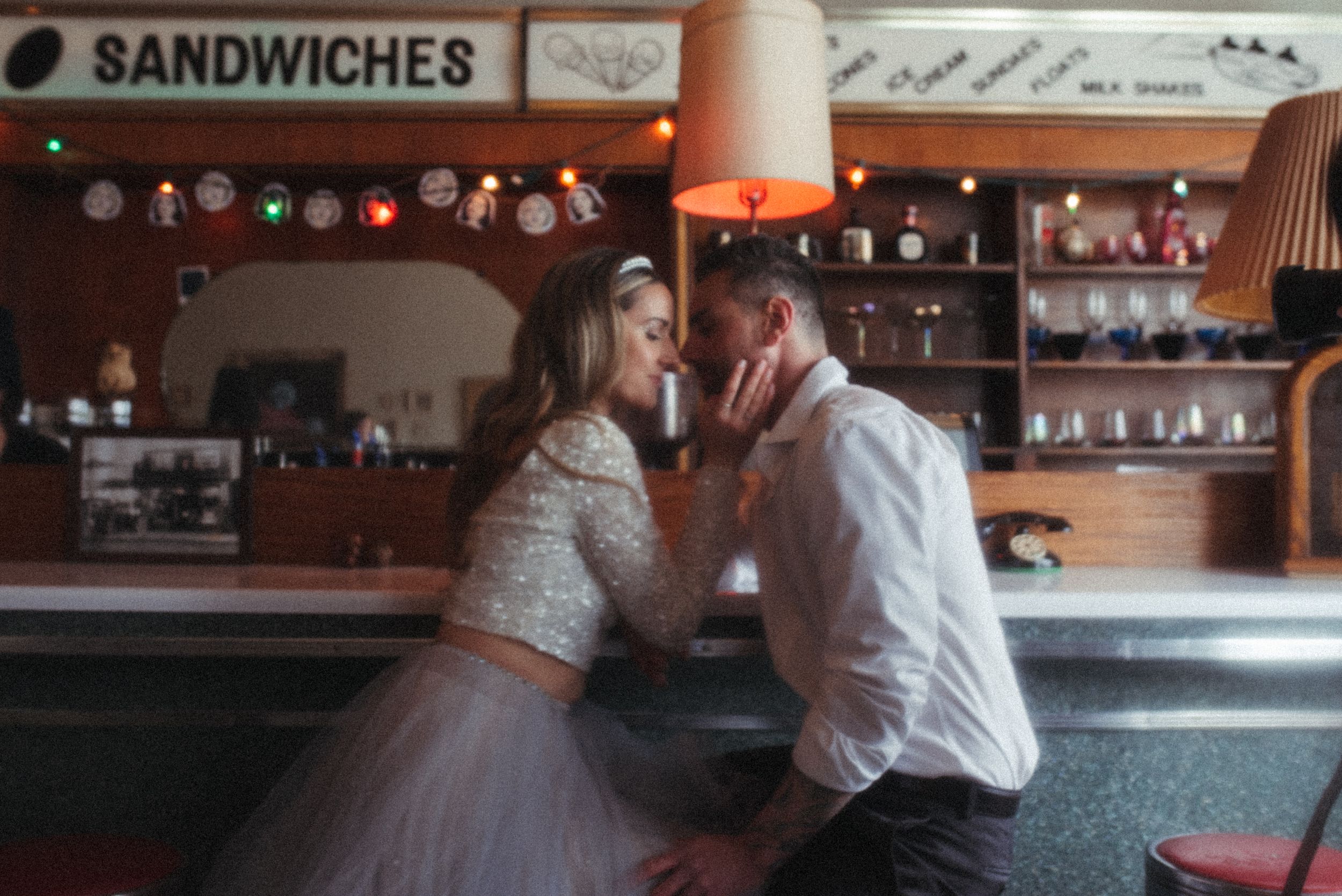 Couple shares intimate moment at retro diner counter with sandwich menu visible.