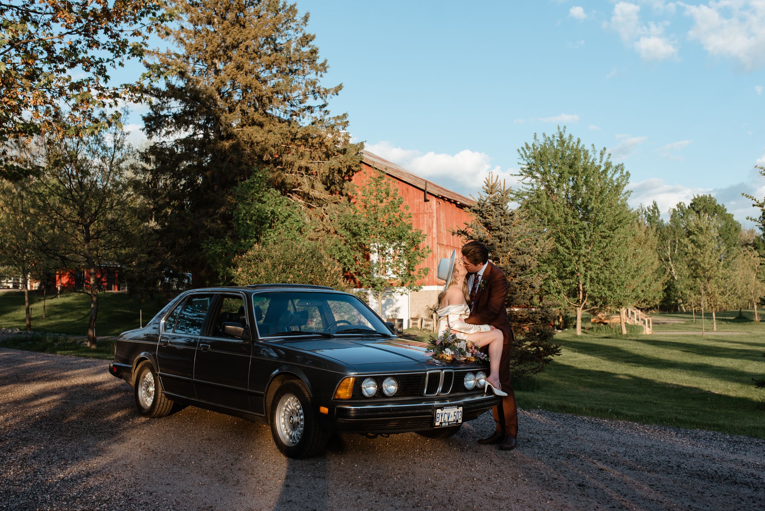 Classic black BMW sedan parked in front of rustic red barn setting.