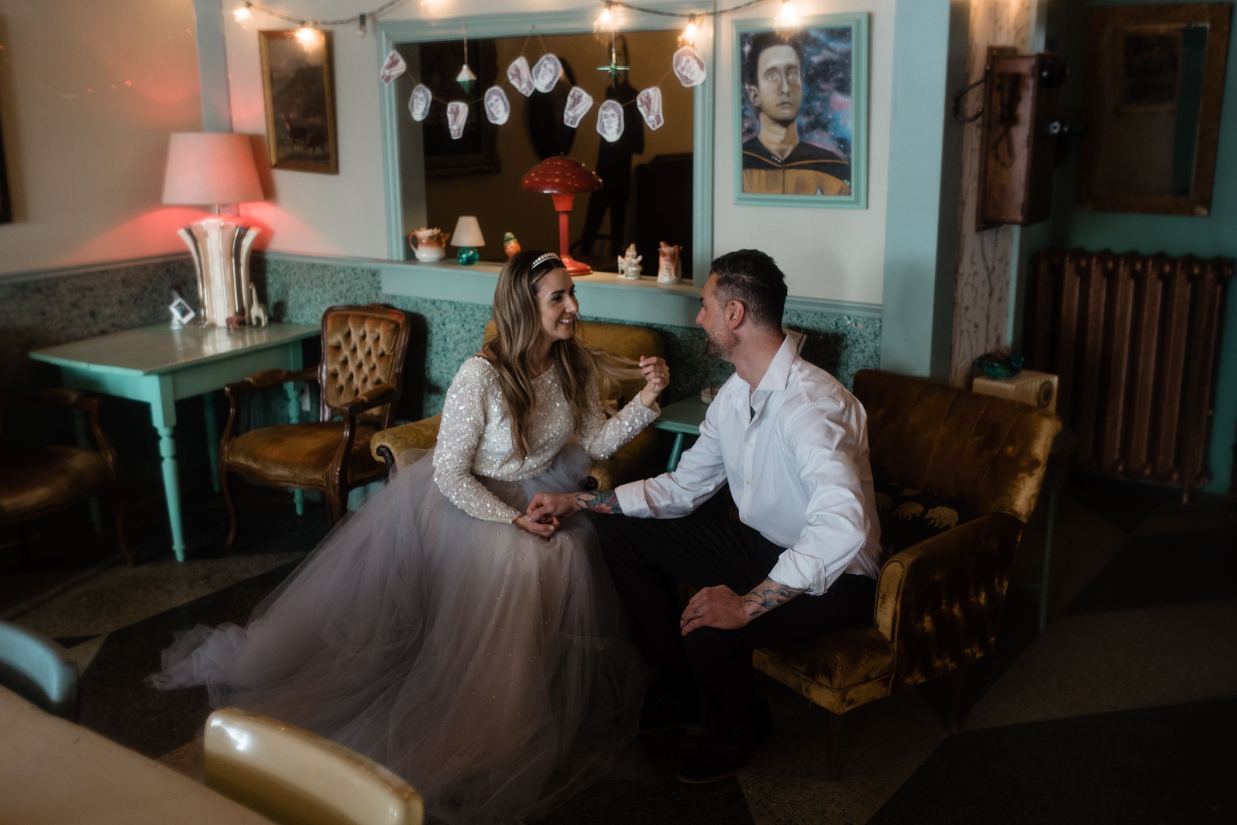 Couple sits in vintage diner booth under twinkling lights and retro decor.