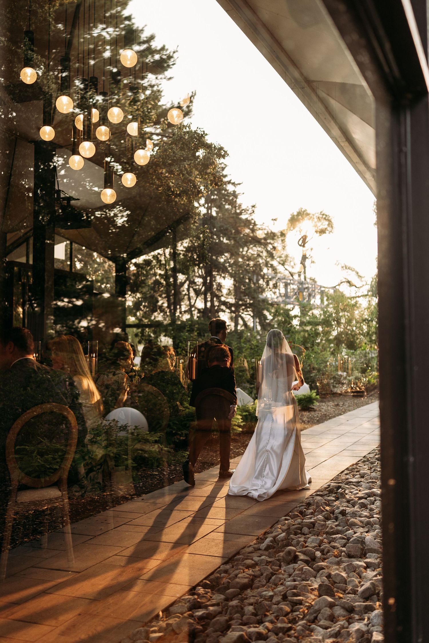 A wedding scene at sunset with hanging string lights and decorative details along a garden path during golden hour.
