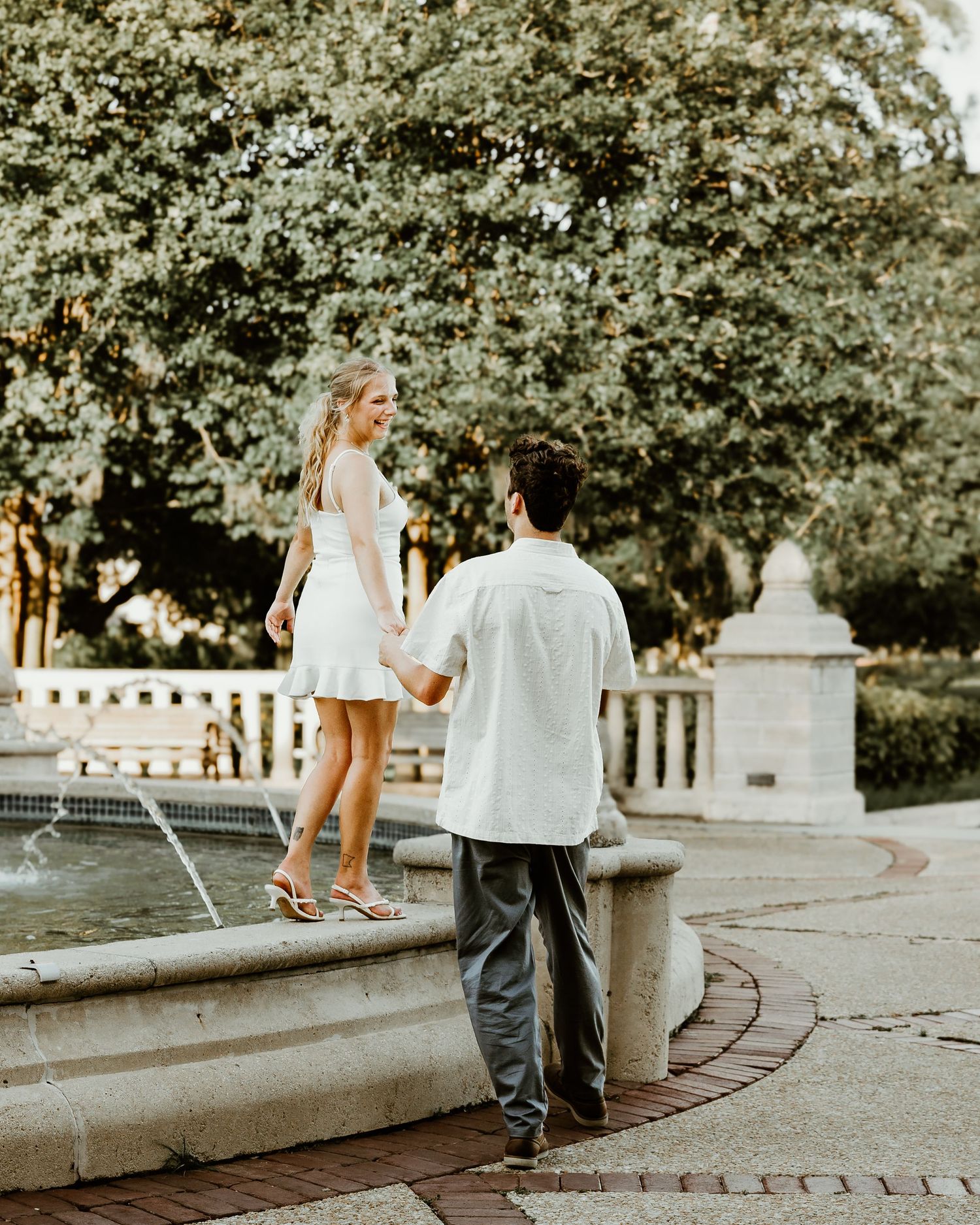 Casual couple walking along a stone pathway surrounded by lush greenery.