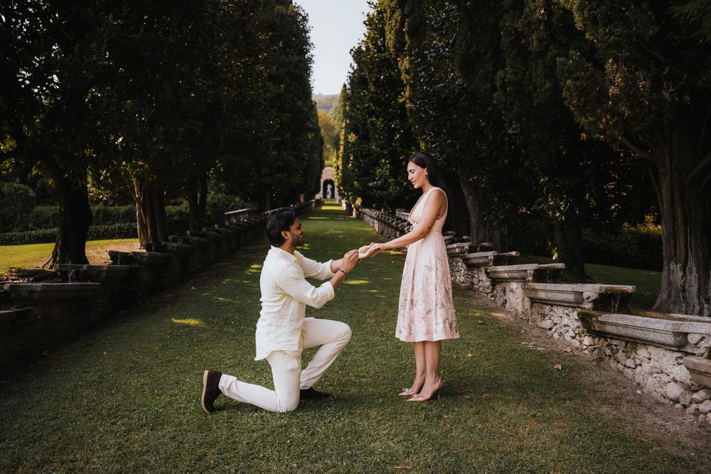 A romantic marriage proposal takes place in a serene garden setting with a stone wall backdrop at sunset.