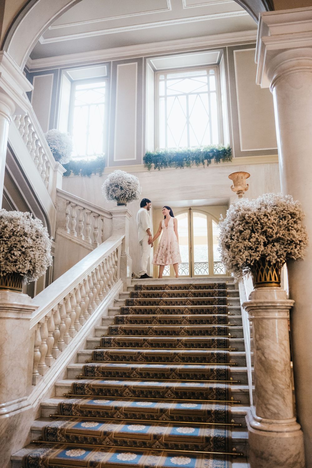 Elegant marble staircase with ornate railings decorated with white floral arrangements in a grand ballroom setting.