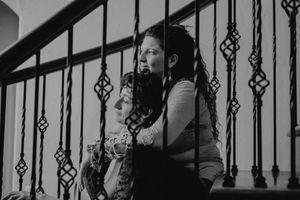 Black and white photo of performer near ornate stair railing during indoor event.