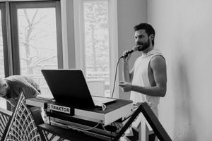 Professional musician performs at an electronic keyboard setup in a bright room with windows.