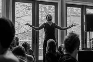 Dynamic black and white shot of a performer with arms outstretched against bright windows.