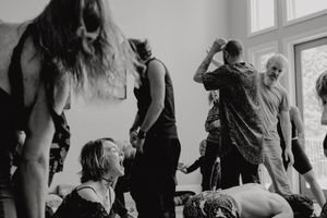 A black and white image of people dancing and moving in a bright room with windows.