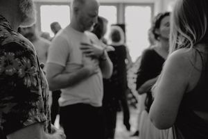 Black and white photo of people gathered in a bright room with windows during a casual dance event.