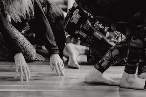 Close-up black and white shot of hands and feet on a wooden floor during movement practice.