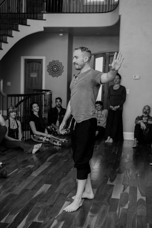 Instructor demonstrating a dance move in a studio space with wooden floors and watching students.