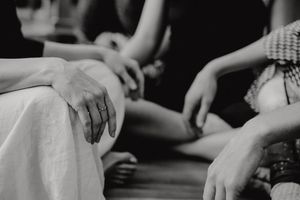 A close-up black and white image of hands resting on fabric.