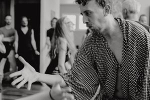 Dancer in patterned shirt gesturing expressively during a studio rehearsal.