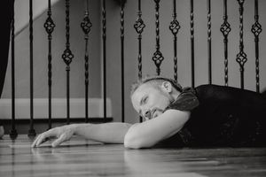 Black and white portrait of person lying dramatically on floor near decorative railings.